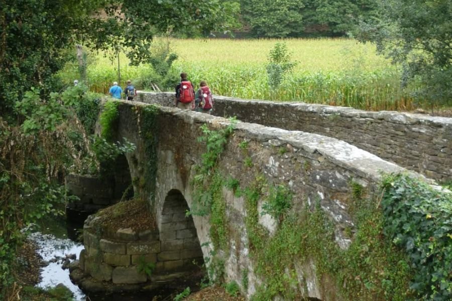 Peregrinos atravessando uma ponte medieval de pedra no Caminho entre Sarria e Santiago de Compostela