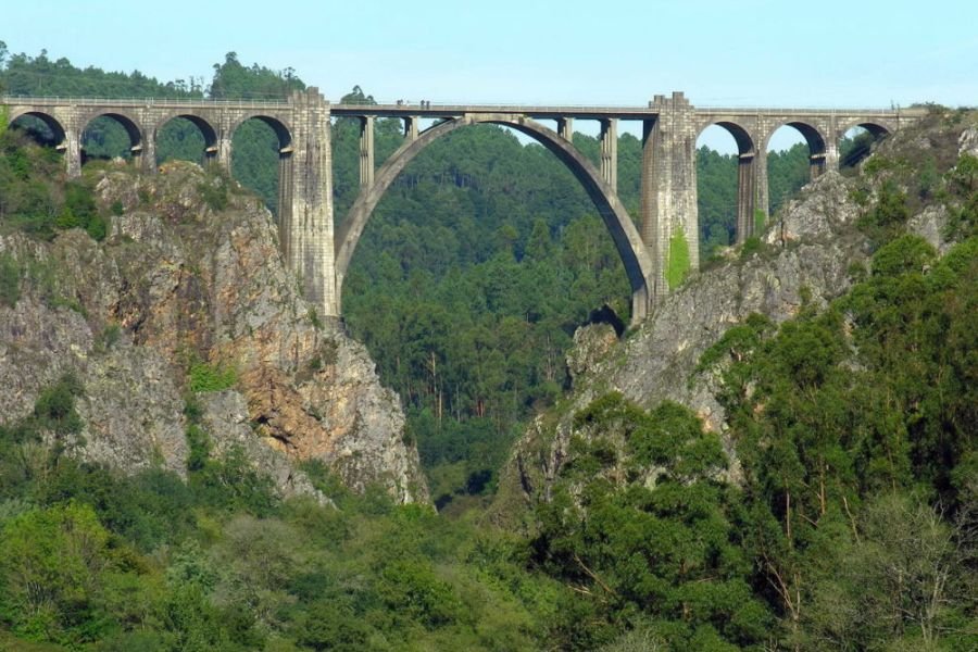 Ein hohes steinernes Eisenbahnviadukt mit großem Mittelbogen über einer bewaldeten Schlucht im Ulla-Tal, bei Ponte Ulla