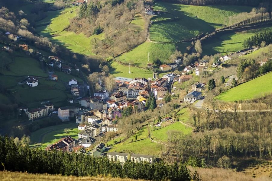Il paese di Pola de Allande in fondo a una verde valle, circondato da prati e boschi