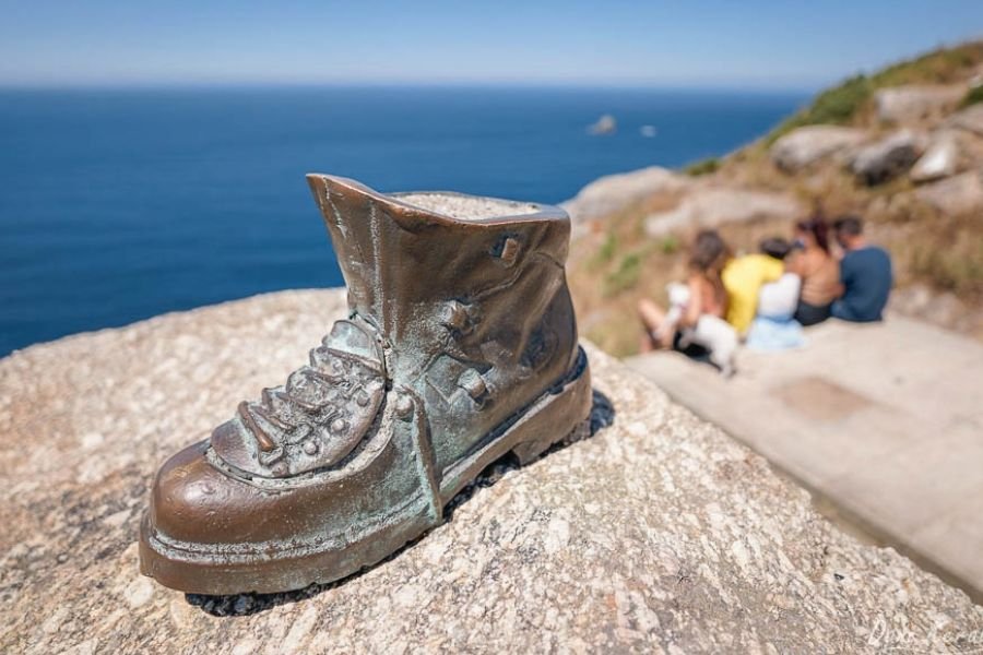 Una bota de peregrino de bronce sobre una roca en el Cabo Finisterre, con el Atlántico azul al fondo