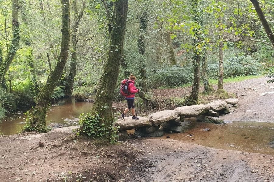 Una peregrina cruzando un arroyo sobre una losa de piedra, en los bosques de Galicia
