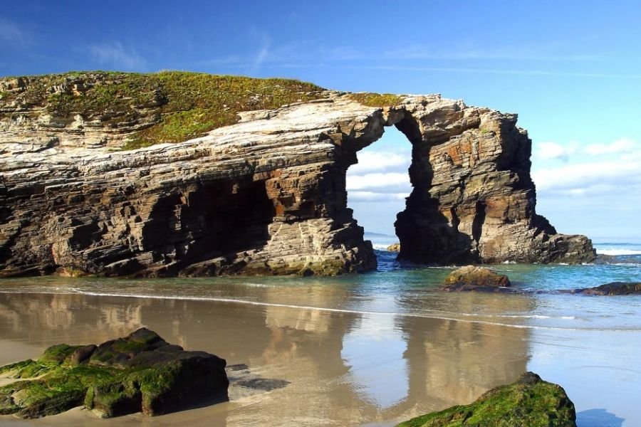 The rock arches of Las Catedrales Beach near Ribadeo, reflected in the wet sand at low tide