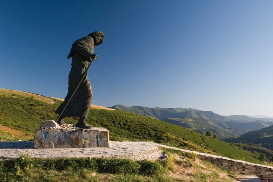 The bronze pilgrim statue leaning into the wind at the Alto de San Roque, with the Galician mountains behind
